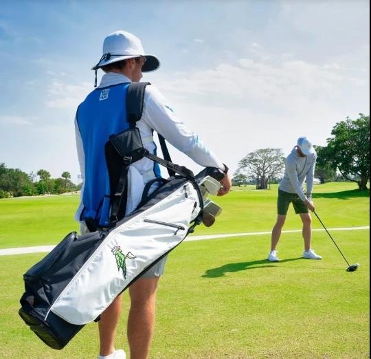 A golfer getting ready to swing, while a caddy stands nearby with a golf bag