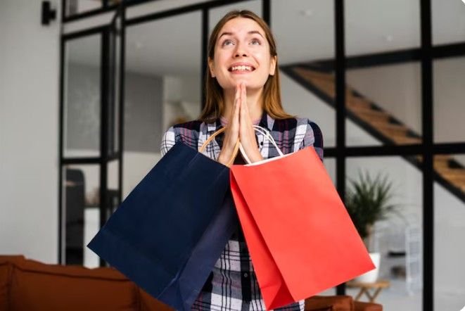 A happy woman smiling with two shopping bags, one red and one blue.